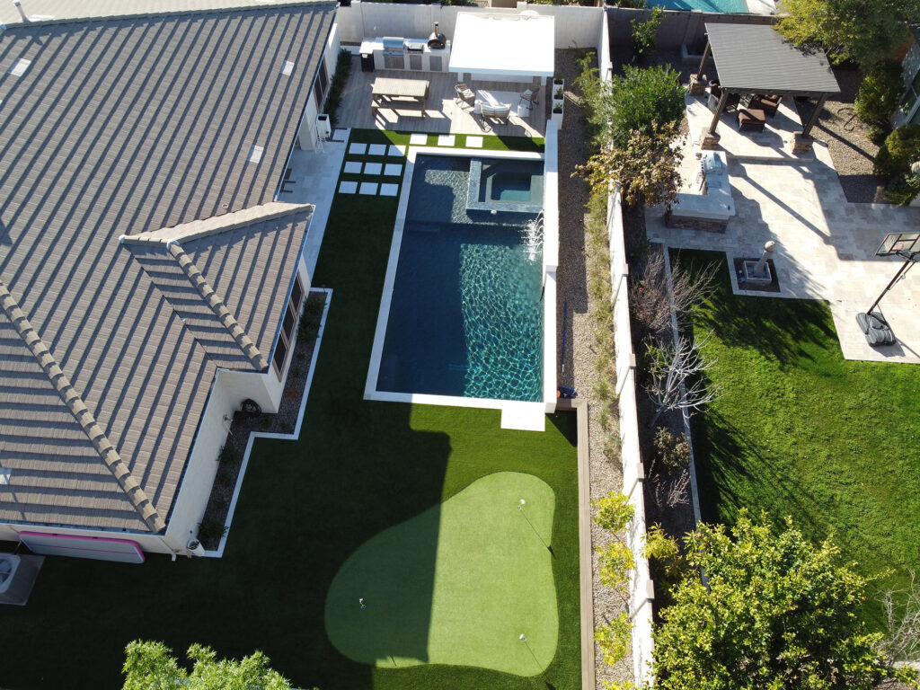 Aerial view of a Phoenix home with a modern backyard featuring a rectangular pool, raised spa, artificial turf patterns and paver walkways designed by pool builders.