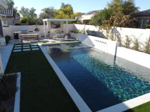 Thumbnail of http://Soft-focus%20view%20of%20an%20Arizona%20backyard%20with%20white%20retaining%20walls,%20artificial%20turf,%20and%20a%20covered%20lounge%20area%20designed%20by%20pool%20contractors%20in%20Phoenix.