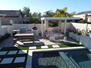 Thumbnail of http://Modern%20backyard%20in%20Phoenix,%20Arizona%20featuring%20a%20sleek%20rectangular%20pool%20with%20spa,%20artificial%20turf%20and%20white%20paver%20paths,%20plus%20a%20pergola-covered%20outdoor%20kitchen%20and%20bar%20area%20designed%20by%20professional%20pool%20builders.