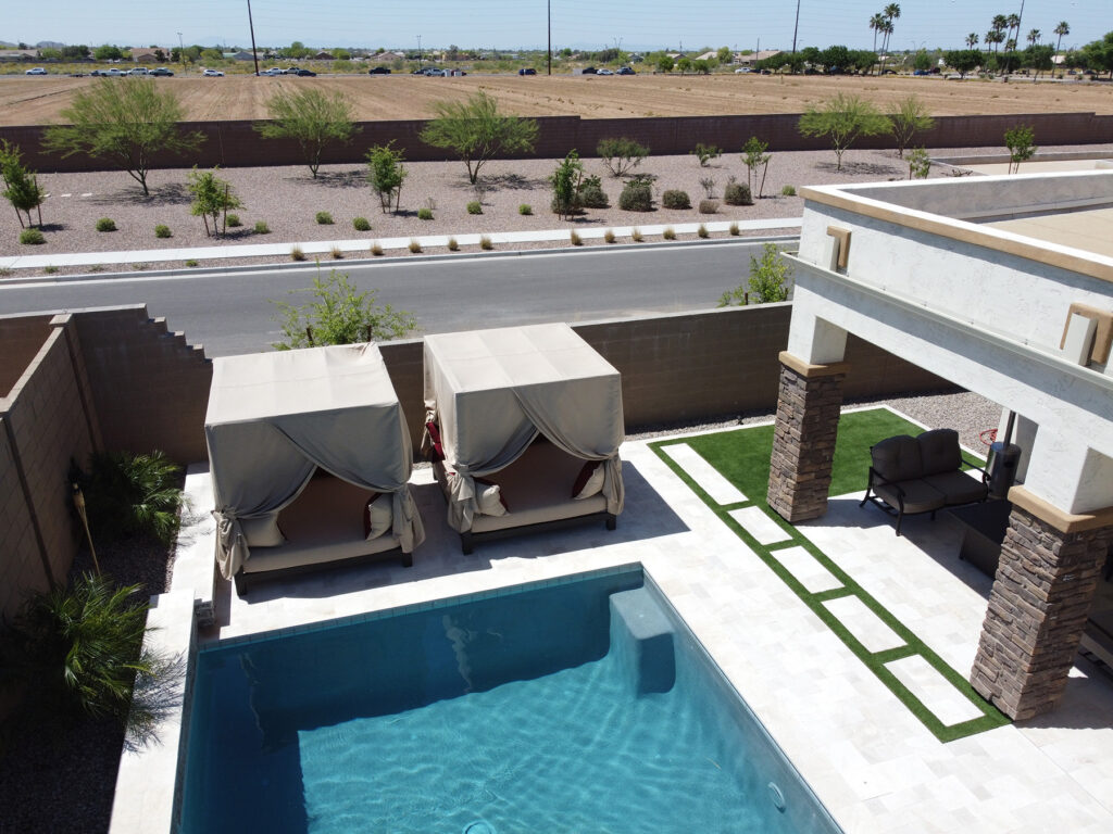 Side view of a rectangular Arizona pool with cabanas, pergola, and green turf accents beside a road, built by Phoenix pool companies.