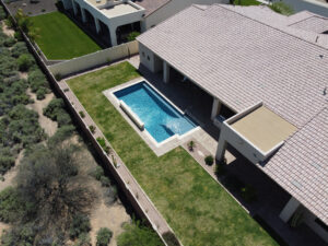 High-angle view of an Arizona property with a rectangular lap pool along the house, landscaped lawn, and desert terrain, designed by pool builders in Phoenix.
