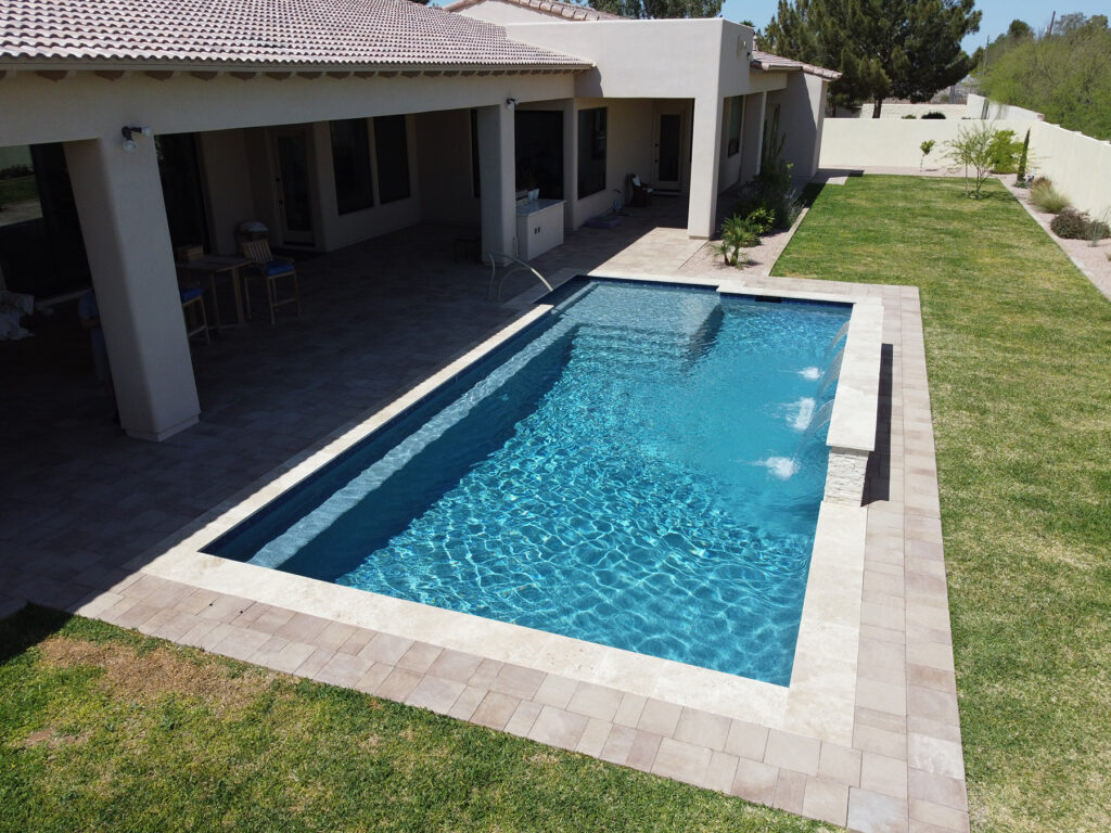 Angled view of a rectangular lap pool with paver deck and grassy yard beside a modern home in Arizona, built by pool builders in Phoenix.