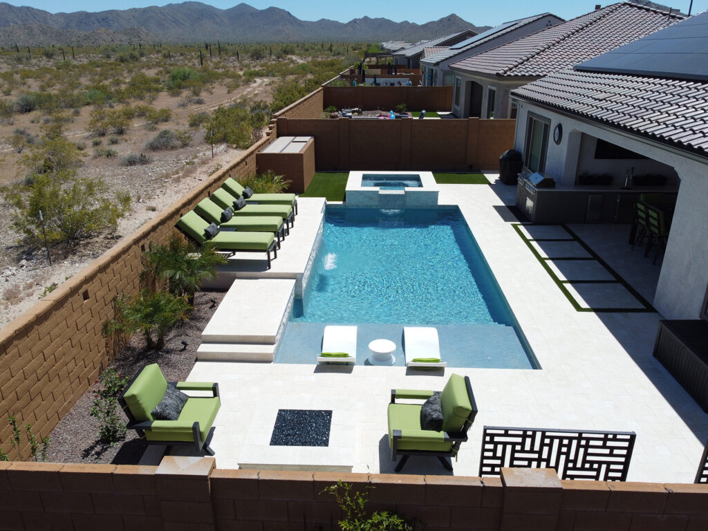 Elevated view of a modern backyard in Phoenix, Arizona featuring a rectangular swimming pool with a built-in spa, green lounge chairs, and desert landscaping by experienced pool builders.