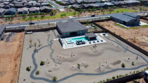 Wide aerial view of a large Arizona property featuring a contemporary house with a turquoise rectangular pool and patio, surrounded by a vast desert yard with winding gravel paths and young trees, built by Phoenix pool builders.