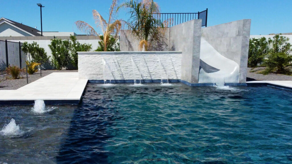 Modern Arizona swimming pool with dramatic white water feature walls and cascading spillway, dark blue water and deck jets in a Phoenix backyard built by pool contractors.