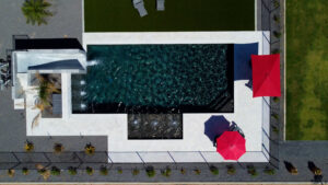Aerial view of modern geometric pool complex with long lap pool, shallow wading pool, red umbrellas and travertine deck in Scottsdale Arizona built by Caribbean Pools