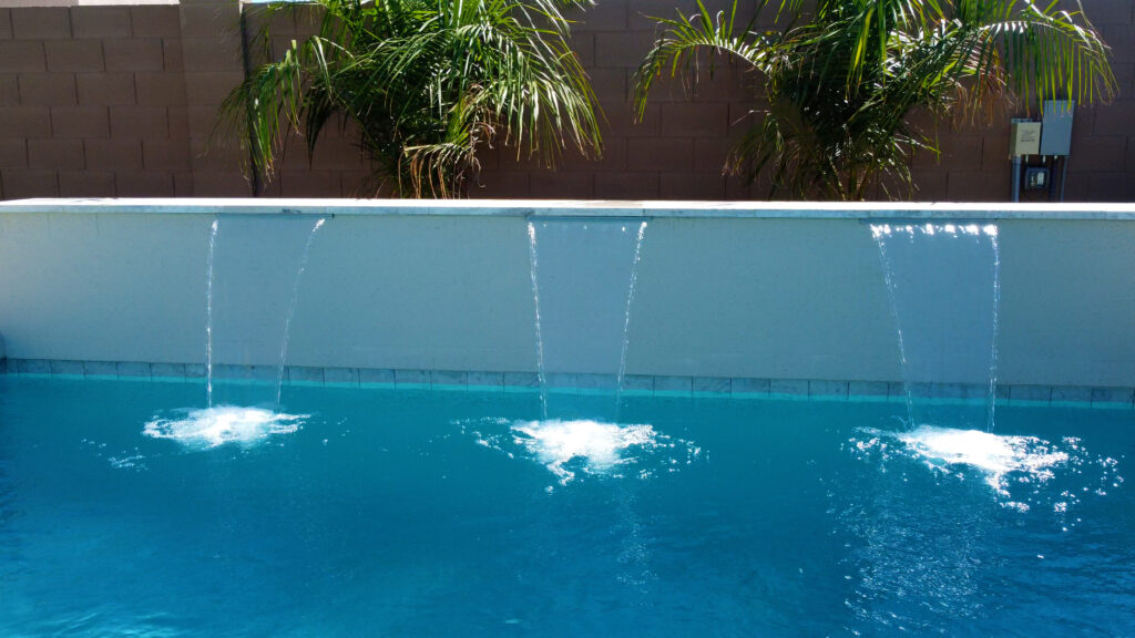 Close-up of pool water feature with three laminar jets cascading into blue pool against a backdrop of palm trees and privacy wall in Phoenix Arizona built by Caribbean Pools