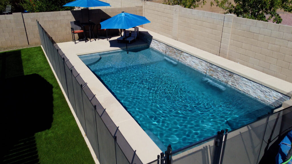 Long narrow lap pool with safety fence, blue sun umbrellas and stone coping in Mesa Arizona built by Caribbean Pools