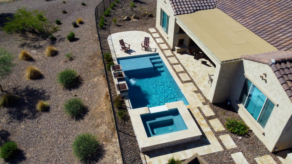Aerial oblique view of rectangular lap pool and attached elevated spa with travertine deck and desert landscape at Gilbert Arizona home built by Caribbean Pools