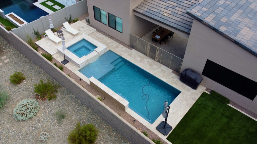 Aerial view of narrow side-yard lap pool with attached raised spa and travertine deck next to modern home and artificial lawn in Paradise Valley Arizona built by Caribbean Pools