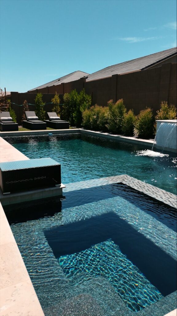 Elegant raised spa spilling into swimming pool with water feature and chaise lounges in Phoenix Arizona built by Caribbean Pools