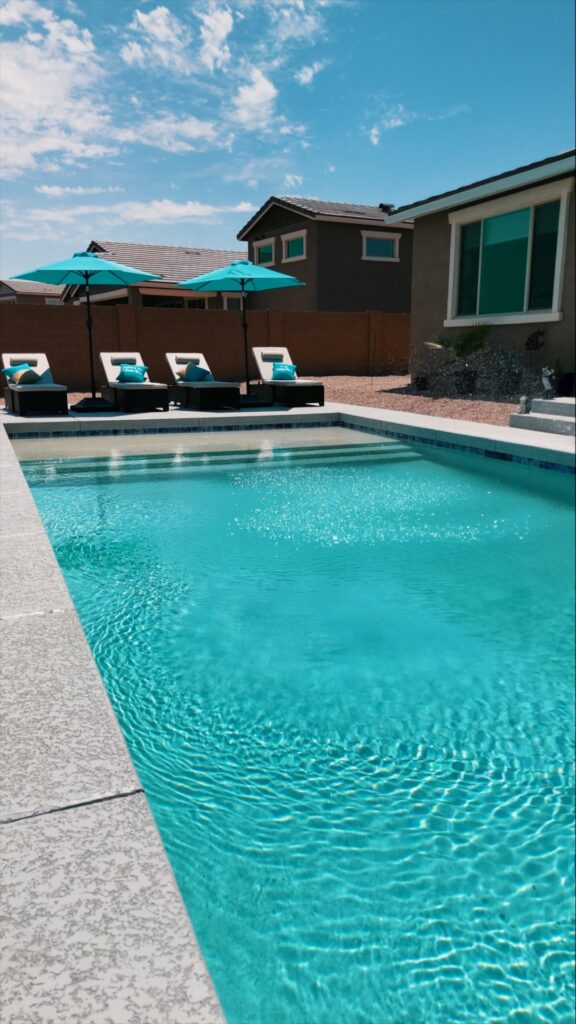 Sparkling rectangular pool with travertine deck and turquoise loungers in Gilbert Arizona backyard by Caribbean Pools